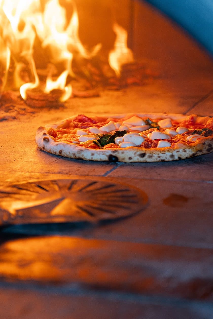 Pizza in the oven mouth, flames climbing the back wall